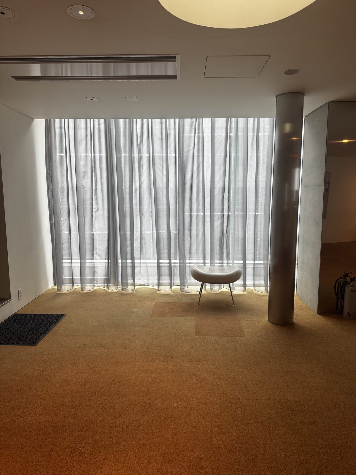 Un piano di Musashino Place pieno di luce morbida, una sedia tonda accanto a una finestra con la tenda