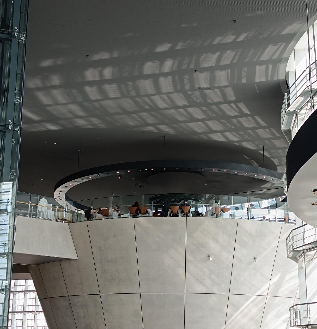 Il soffitto dell'atrio del National Art Center di Tokyo coperto dalle ombre a griglia dei frangisole, sopra l'anello di tavolini del Salon de Thé Rond